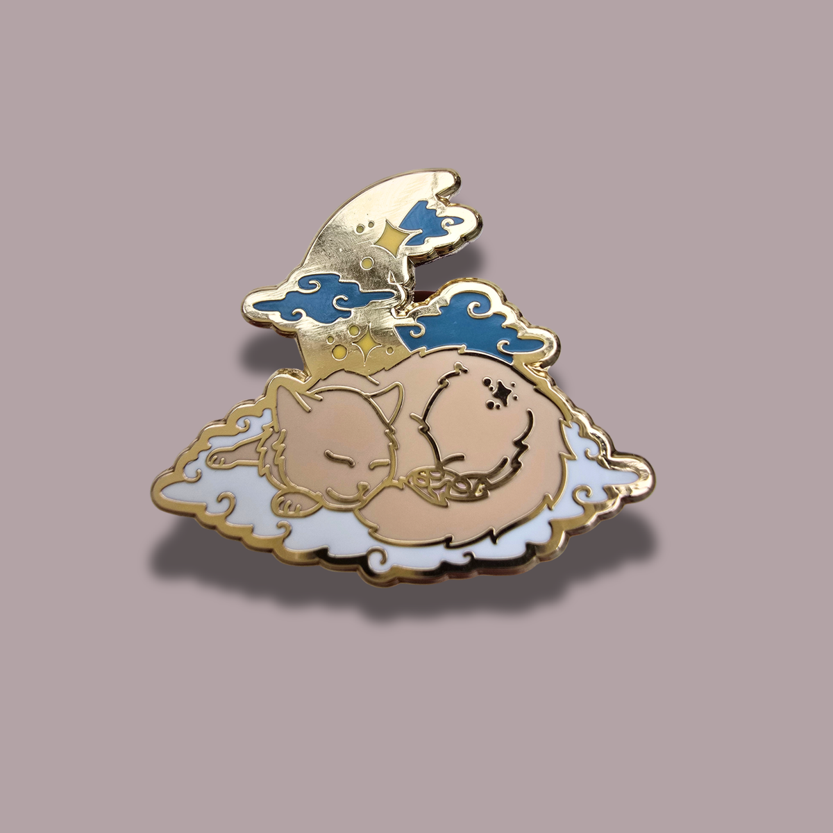 A decorative enamel pin featuring a sleeping cat curled up on a cloud, with a crescent moon and blue clouds above, shown on a plain mauve background.