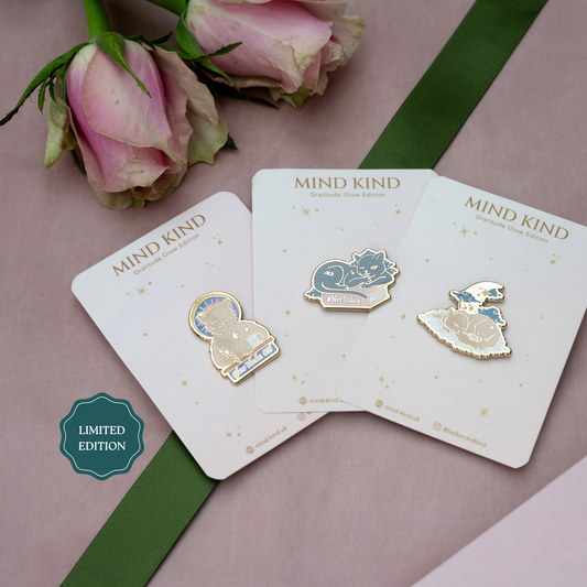Three enamel pins on white display cards with the text 'MIND KIND' and a teal 'LIMITED EDITION' badge, styled with pink roses and a green ribbon on a dusty pink background.
